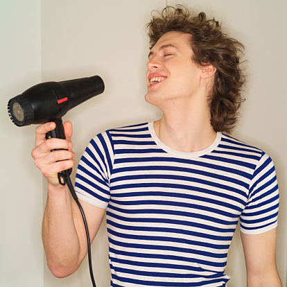 Young man holding hair dryer to face, smiling